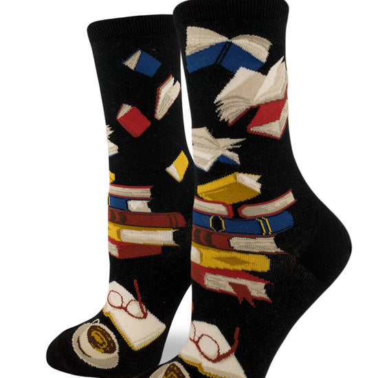 Black crew socks for women with stacked multicolored books and airborne books above, with open book, glasses and cup and saucer below.