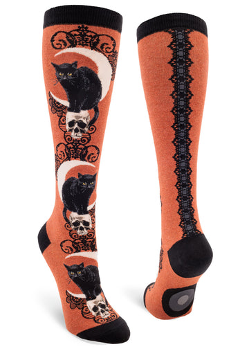 Rust orange knee-high socks with black cats, skulls, crescent moons and lace patterns as well as a faux lace ribbon back seam.
