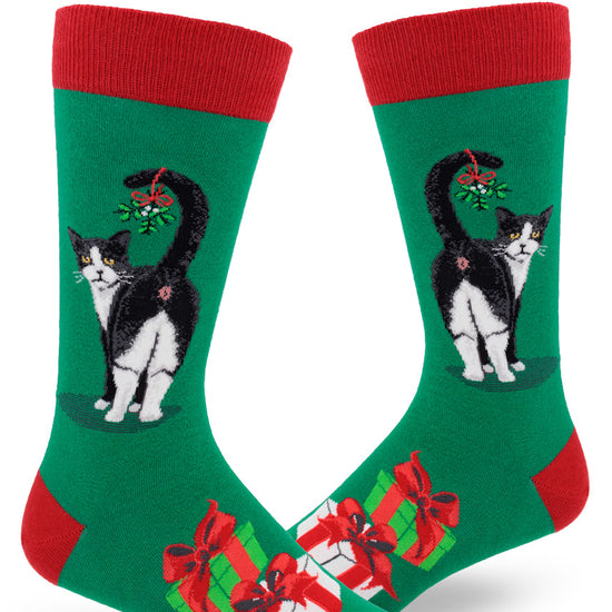 Green men's crew socks with red accents and black and white cat showing its butt with mistletoe hanging from its tail, and presents below.