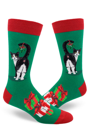Green men's crew socks with red accents and black and white cat showing its butt with mistletoe hanging from its tail, and presents below.