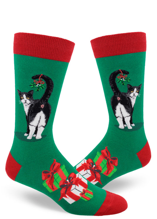 Green men's crew socks with red accents and black and white cat showing its butt with mistletoe hanging from its tail, and presents below.