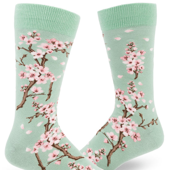 Light green crew socks for men with cherry blossom design of lowers and falling pink petals.