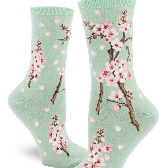 Light green crew socks for women with cherry blossom design of pink flowers and falling petals.