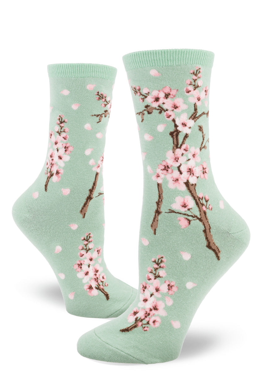 Light green crew socks for women with cherry blossom design of pink flowers and falling petals.