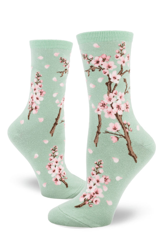 Light green crew socks for women with cherry blossom design of pink flowers and falling petals.