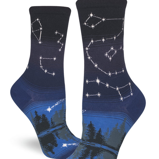 Blue crew socks for women with star constellations and shooting stars above a night forest and reflective lake.