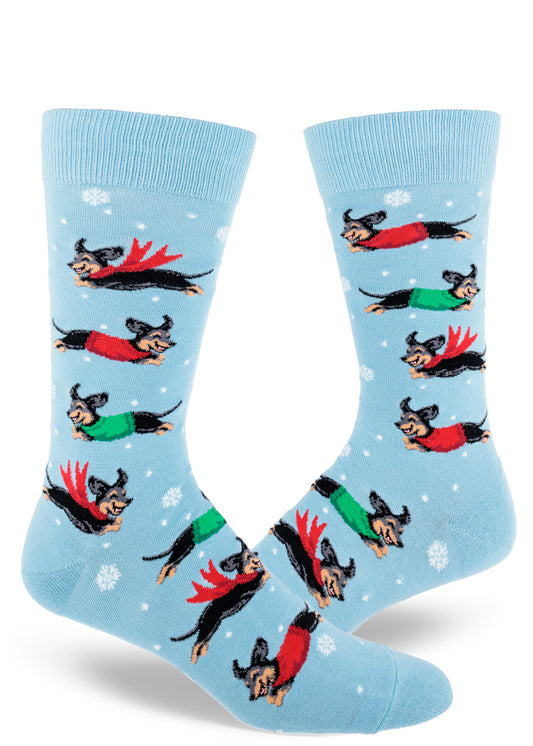Light blue crew socks for men with black and tan dachshunds wearing red and green scarves and sweaters and jumping between snowflakes.
