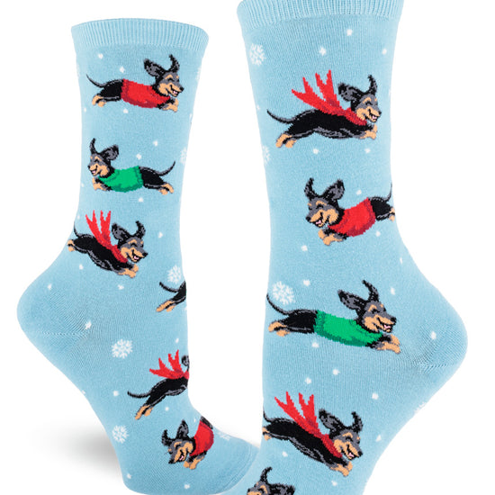 Light blue crew socks for women with black and tan dachshund dogs wearing sweaters and surrounded by snowflakes.