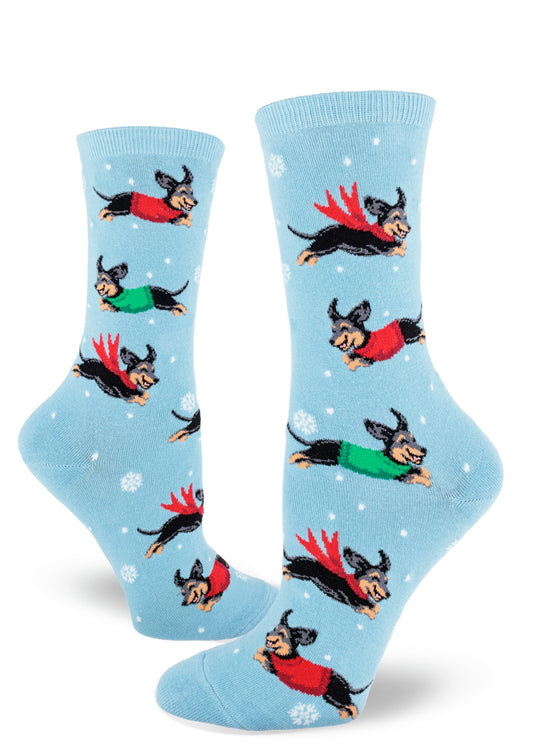 Light blue crew socks for women with black and tan dachshund dogs wearing sweaters and surrounded by snowflakes.