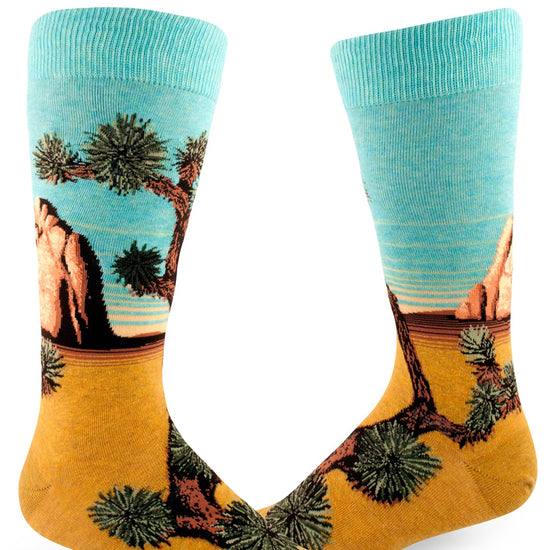 Men's crew socks with the words "Joshua Tree National Park" on the foot and scenery with Joshua trees, rock formations, blue sky and yellow sand.
