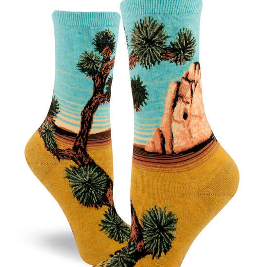 Crew socks for women with "Joshua Tree National Park" at the toe and Joshua trees, rock formation and scenic view of blue sky and yellow sand.