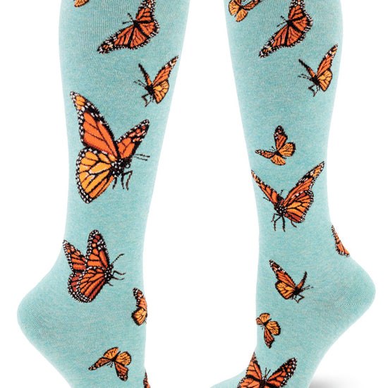 Light blue knee-high socks with orange monarch butterflies in flight in an allover pattern.