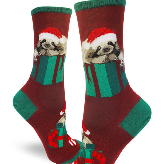 Red crew socks for women with sloths in Santa hats lying on top of green Christmas presents.