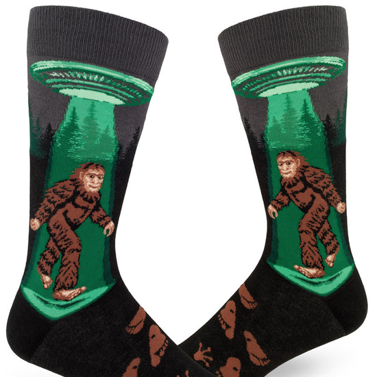 Charcoal men's crew socks with Sasquatch walking under a flying saucer with a green glowing beam, alien and humanoid footprints.