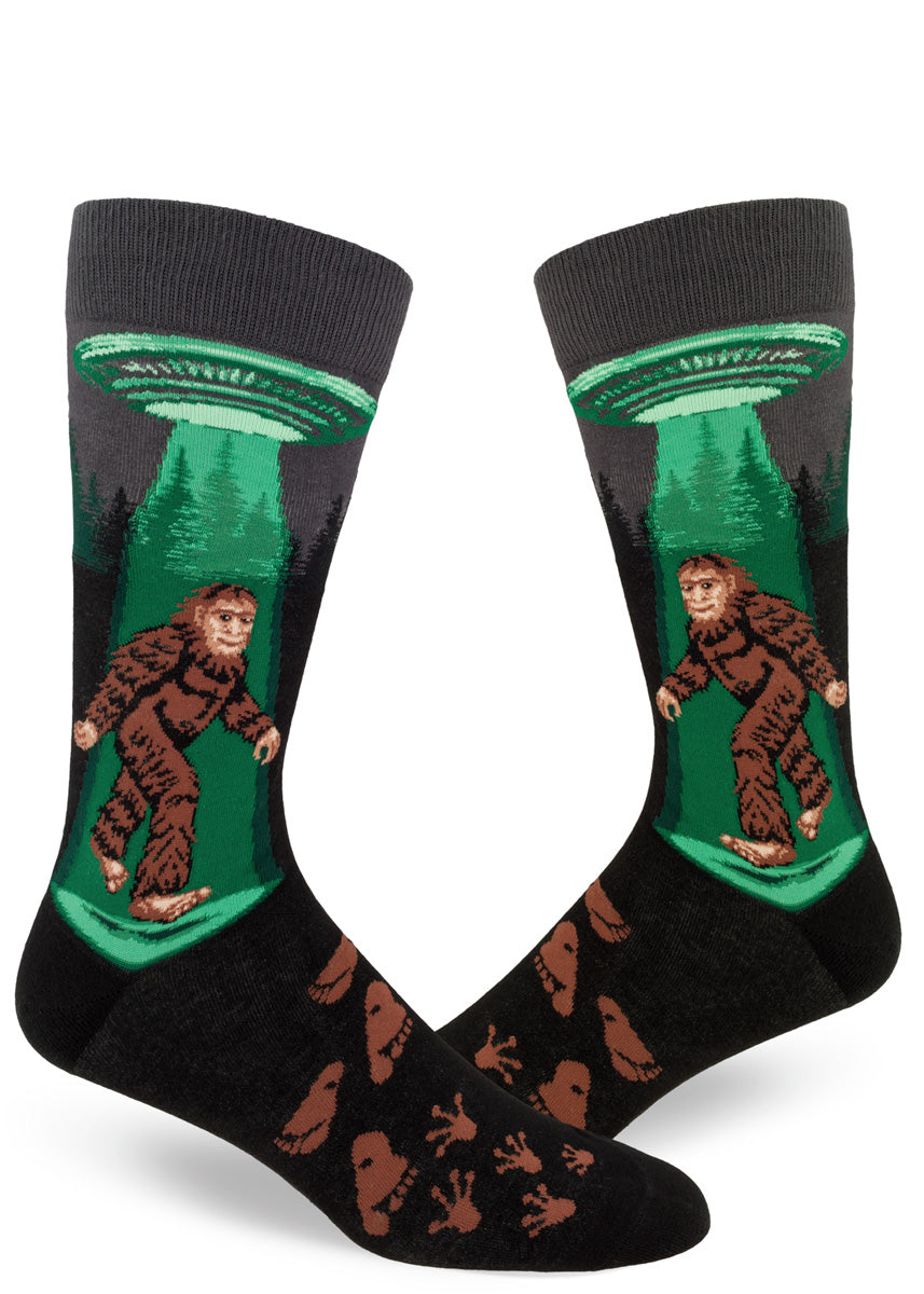 Charcoal men's crew socks with Sasquatch walking under a flying saucer with a green glowing beam, alien and humanoid footprints.
