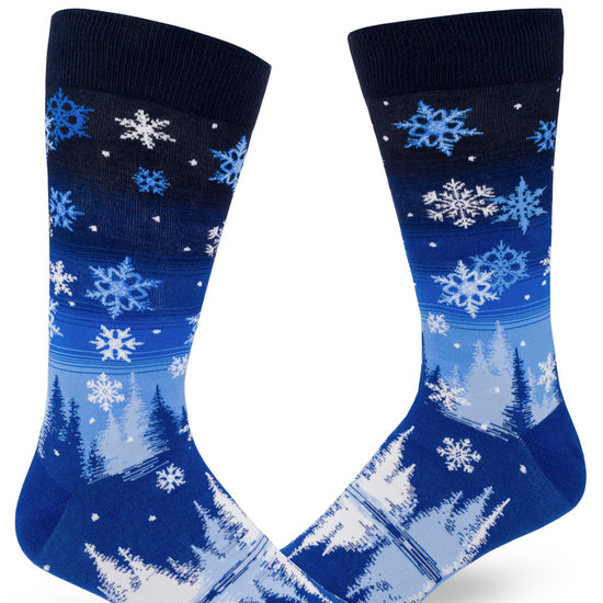 Blue gradient men's crew socks with allover snowflake design that shows snow falling through a night sky over trees above a reflective pond.