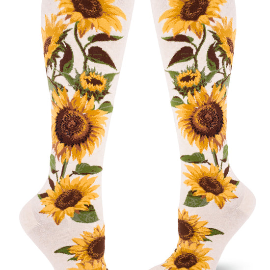 Cream colored knee-high socks featuring bold realistic sunflowers with yellow petals and brown centers and green foliage.