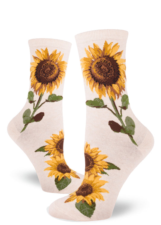 Cream colored crew socks for women with a sunflower design that shows large realistic flowers with yellow petals and brown centers, and green leaves and stems.