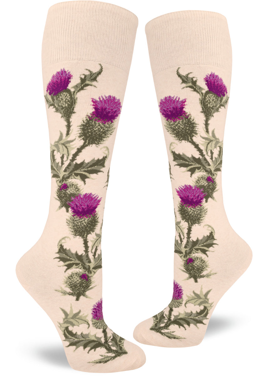 Cream colored knee socks show a floral pattern with realistic purple thistles  and spiky green leaves and stems that grow up along the sides of the socks.